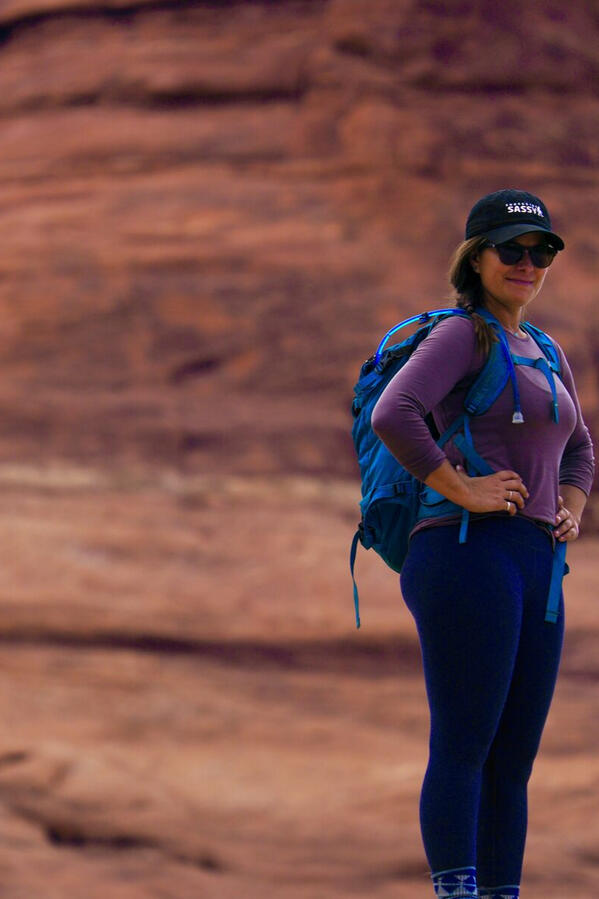 Hiker in a blue pack and Sassy cap smiling against red rock